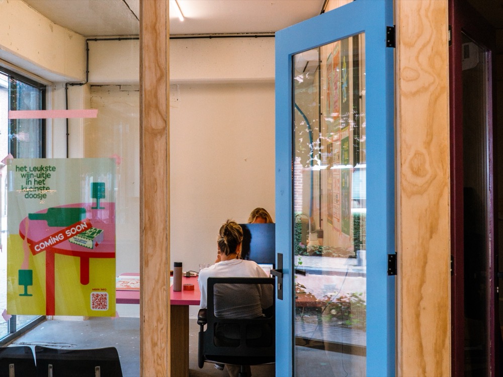 Iemand aan het werk in een atelier bij Dees, achter een open blauwe deur.